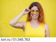 Portrait of a happy woman in sunglasses on a yellow background. Red-haired carefree girl in a dress and earrings tassels of the same color. Lady with an impeccable dazzling smile. Summer photo. Стоковое фото, фотограф Михаил Решетников / Фотобанк Лори