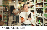 Young female customer in supermarket examines bottles of wine, chooses alcoholic drink.Young female customer in supermarket examines bottles of wine, chooses alcoholic drink. Attentive customer meticulously studies goods in self-service store. Стоковое видео, видеограф Яков Филимонов / Фотобанк Лори