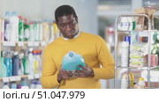 African man customer takes out various product options from shelf and selects liquid detergent. Client carefully examines product, makes purchase decision, doubts correctness of choice. Стоковое видео, видеограф Яков Филимонов / Фотобанк Лори