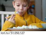 6 years old boy eats pasta with cheese from blue plate. Child is eating spaghetti. Lunch time. Good appetite. Tasty children food. Close-up portrait. Carbs dinner. Fast food. Kid eating with fork. Стоковое фото, фотограф Марина Демидюк / Фотобанк Лори