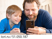 Father and son little boy laughing and using phone. They watching funny videos together, playing games on smartphone. Concept technology, smart phone addicted. Fun weekend activity. Modern fatherhood. Стоковое фото, фотограф Марина Демидюк / Фотобанк Лори
