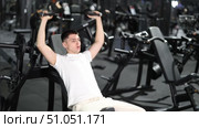 Driven young man training on shoulder press machine in modern well-equipped gym, focused on working deltoids, building upper body strength and staying committed to fit lifestyle. Стоковое видео, видеограф Яков Филимонов / Фотобанк Лори