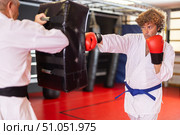 Man in white kimono punches and kicks punching bag held by trainer. Стоковое фото, фотограф Яков Филимонов / Фотобанк Лори