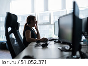Tired woman in a black T-shirt works in an empty office and yawns at the workplace. The girl works overtime and is very tired. Female silhouette on a window background. Boring monotonous routine. Стоковое фото, фотограф Михаил Решетников / Фотобанк Лори