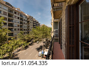 A sunny street view from a balcony in a city. Buildings line the street, with trees providing shade. Clear blue sky enhances the urban landscape. Стоковое фото, фотограф PAv / Фотобанк Лори