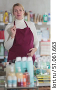 Young pregnant saleswoman wearing burgundy apron standing in personal care and cleaning supplies store aisle, smiling and gesturing warmly, welcoming customers to shopping. Стоковое видео, видеограф Яков Филимонов / Фотобанк Лори