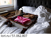 Open suitcase with clothes on unmade hotel bed by a window. Стоковое фото, фотограф Lamina Akulova / Фотобанк Лори