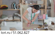 In workshop, woman designer draws diagram of future clothing product on paper. Creating dress pattern according to individual sizes, preparatory stage of work in sewing production. Стоковое видео, видеограф Яков Филимонов / Фотобанк Лори