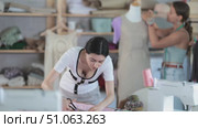 Dedicated female tailor cutting soft pink fabric into pattern pieces, building foundation for new custom garment in workshop, while teammate adjusting sample dress on mannequin. Стоковое видео, видеограф Яков Филимонов / Фотобанк Лори