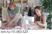 Mature dressmaker draws patterns of clothes on paper using curved rulers while an assistant seamstress works on a sewing machine. Стоковое видео, видеограф Яков Филимонов / Фотобанк Лори