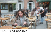 On open area of cafe, girl in restaurant eating salad. Single client sits at table, eats and enjoys views of ancient European city around. Стоковое видео, видеограф Яков Филимонов / Фотобанк Лори