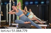 Young woman sitting on box set bed reformer, performs tilt exercise for abdominal muscles. Athlete participates in pilates training. Strength workout for various muscle groups using sports equipment. Стоковое видео, видеограф Яков Филимонов / Фотобанк Лори