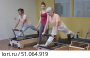 Senior woman doing exercises on reformer in pilates studio with young female personal trainer controlling her movements. Стоковое видео, видеограф Яков Филимонов / Фотобанк Лори