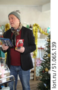 Mature man pulls a razor and a hair trimmer in his hands and chooses which one to take. Man buying razors on the background of a Christmas tree in a supermarket. Стоковое видео, видеограф Яков Филимонов / Фотобанк Лори