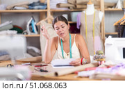 Young tailoress engaged in paperwork in sewing workshop. Стоковое фото, фотограф Яков Филимонов / Фотобанк Лори