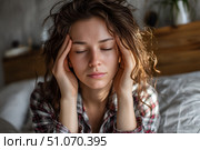 Красивая молодая женщина с головной болью сидит на диване, обхватив голову обеими руками и слегка щурясь от боли. Крупный план. Стоковое AI-изображение, AI-художник Максим Коломыченко / Фотобанк Лори