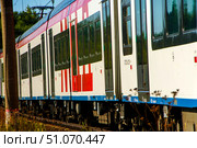 An IDC train with red and white stripes is moving along the rails in a suburban area. Russia. Moscow oblast. 14.08. 2025. Редакционное фото, фотограф Ярославский Максим / Фотобанк Лори