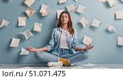 A woman sits in a blue room, meditating while papers fly around her. Стоковое AI-видео, аниматор Данила Большаков / Фотобанк Лори