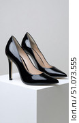 Pair of black patent leather high heels on white cube. Стоковое AI-изображение, AI-художник Юрий Поздников / Фотобанк Лори