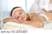 Smiling young woman relaxing on massage table in spa salon while skilled female therapist performing anti-cellulite thigh and butt massage. Стоковое видео, видеограф Яков Филимонов / Фотобанк Лори