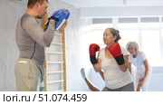 Elderly woman with her trainer at gym. Woman wearing boxing gloves exercise and punch to pads for boxing. Стоковое видео, видеограф Яков Филимонов / Фотобанк Лори