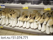 A shelf in a shoe store with neatly laid out women's winter boots. The model is made of white leatherette with an internal insulation of beige artificial fur. The boots have a medium height shaft, decorative lacing on the side and a cuff showing off the soft fur. The sole is made of durable brown material. Each pair is equipped with an anti-theft tag. The shoes are arranged in rows, creating a neat and attractive look of the display case. A price tag with a price of 1999 rubles is visible on the shelf. (2015 год). Редакционное фото, фотограф Анна Кривицкая / Фотобанк Лори