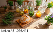 Homemade sourdough bread on a cutting board with herbal infusions and citrus drinks in jars. Rustic table setting with natural healthy food and drinks at summer. Стоковое AI-изображение, AI-художник Анжелика Самсонова / Фотобанк Лори