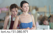 Careful female dressmaker measuring young woman while assistant sewing in tailor workshop. Стоковое видео, видеограф Яков Филимонов / Фотобанк Лори