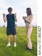 Man exercising with resistance bands while woman takes notes on workout routine outdoors. Стоковое фото, фотограф Raquel Corcoles Mendez / Фотобанк Лори