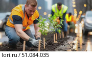 Three men planting young trees in a city street. They wear safety vests and gloves. The scene shows urban greening efforts and environmental care. Стоковое AI-видео, аниматор Nart / Фотобанк Лори