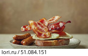 A plate of breakfast featuring two fried eggs, crispy bacon, and sausages. The bacon appears to be floating above the eggs, creating a dynamic visual effect. Стоковое AI-видео, аниматор Nart / Фотобанк Лори