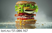 A towering burger with layers of lettuce, cheese, bacon, pickles, and tomatoes on a sesame seed bun. The background is blurred, emphasizing the burger's details. Стоковое AI-видео, аниматор Nart / Фотобанк Лори