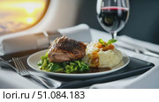 A gourmet meal served on an airplane tray. The dish includes grilled chicken, mashed potatoes, and sautéed greens. A glass of red wine is beside it. Стоковое AI-видео, аниматор Nart / Фотобанк Лори