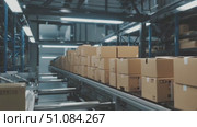 A modern warehouse interior with a conveyor belt transporting numerous cardboard boxes. The environment is well-lit and organized, showcasing efficient logistics operations. Стоковое AI-видео, аниматор Nart / Фотобанк Лори