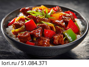 Sweet sour pork with colorful peppers, mixed vegetables served in a black bowl on dark concrete background. Traditional Chinese dish. Close-up. The meat pieces in a brown sauce glaze. Sichuan cuisine. Стоковое AI-изображение, AI-художник Марина Демидюк / Фотобанк Лори