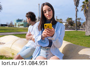 Couple conflict outdoors, woman on phone, man upset. Стоковое фото, фотограф Raquel Corcoles Mendez / Фотобанк Лори