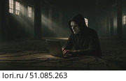 A masked individual sits on the floor of a dimly lit room, using a laptop. Shadows and light beams create a mysterious atmosphere. Стоковое AI-видео, аниматор Nart / Фотобанк Лори