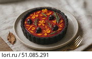A Halloween-themed tart with a dark crust, topped with orange flowers, green leaves, and small skulls. The tart is placed on a neutral-colored plate. Стоковое AI-видео, аниматор Nart / Фотобанк Лори