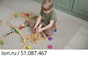 Cute little blonde child boy sitting on the floor playing with wooden toy train. Toddler kid plays railway. Made of natural materials. Birthday gift. Preschool employment. Brain, coordination exercise. Стоковое видео, видеограф Марина Демидюк / Фотобанк Лори