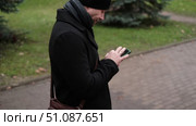 Handsome man wearing black coat and brown leather bag walking down on the city, drinking coffee paper takeaway cup with mobile phone. Stylish bearded middle-aged male using smartphone at urban street. Стоковое видео, видеограф Марина Демидюк / Фотобанк Лори