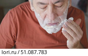 Senior Man shaving his face. Old male shaves beard and mustache with shaver. Elderly gray haired man looking at the mirror, applies shaving cream foam and using razor. Skin hygiene. Daily body care. Стоковое видео, видеограф Марина Демидюк / Фотобанк Лори