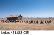 A school in rural Africa with children walking to class, backpacks on, bright blue sky and open landscape. Black African children from disadvantaged families study in school, read books, receive primary education, volunteer service. Стоковое AI-изображение, AI-художник ALLA YURTAYEVA / Фотобанк Лори
