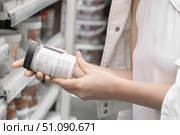 In a home improvement store, a woman dressed in white clothing inspects a jar of paint she has picked up from a shelf. She carefully studies the composition and toxicity details. Стоковое фото, фотограф Владимир Разгуляев / Фотобанк Лори