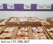 Supermarket counter with chilled chicken meat in packaging. The goods are laid out in yellow trays and packed in transparent film, placed in cardboard boxes. On the wall above the counter, price tags are visible indicating the cost per kilogram: chicken thighs, drumsticks, wings and other parts. Prices range from 119.99 to 144.99 rubles per kilogram. The design of the sales area is minimalist: a white wall with a purple horizontal stripe and standard printed price tags. The scene conveys the atmosphere of a grocery store or hypermarket with an emphasis on the mass sale of fresh chilled poultry meat. (2019 год). Редакционное фото, фотограф Анна Кривицкая / Фотобанк Лори