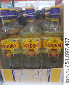 Gordon's London Dry Gin bottle stand. Glass transparent bottles with yellow labels and purple caps are displayed in a row in an open cardboard box. The label depicts the brand logo with a red mythical animal (a boar with a dragon's head), the inscription "The Original Gordon's London Dry Gin". The necks of the bottles are equipped with protective anti-theft devices. The background indicates that the photo was taken in a store or supermarket. The overall appearance emphasizes the corporate style of the Gordon's brand and the atmosphere of the alcoholic beverages department. (2019 год). Редакционное фото, фотограф Анна Кривицкая / Фотобанк Лори