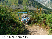 Ala-Archa, trash container filled with plastic bottles and litter stands beside a narrow dirt path, highlighting environmental impact and waste management challenges in popular mountain tourism areas. Стоковое фото, фотограф Андрей Ка / Фотобанк Лори