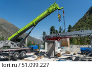 Aerial cableway, Mobile crane hoists gearbox and bullwheel assembly onto station frame, crews align, crates and tools scattered. Transportation upgrade in alpine Ala-Archa gorge camp Kyrgyzstan. Стоковое фото, фотограф Андрей Ка / Фотобанк Лори