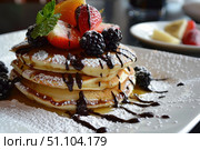 Delicious pancakes topped with fresh fruits and chocolate drizzle for a scrumptious breakfast. Стоковое AI-изображение, AI-художник Иван Рябоконь / Фотобанк Лори