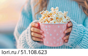 Warm and inviting scene featuring person's hands adorned with pink nail polish, gently cradling decorative pink popcorn cup, while wearing comforting blue knit sweater. Стоковое AI-изображение, AI-художник Данила Большаков / Фотобанк Лори