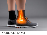 Leg with ankle joint pain icon. Foot wearing running shoes showing the bones in the ankle area. Grey floor. Feet with red effect of painful injury problems. Legs with anatomical detail glowing orange. Стоковое AI-изображение, AI-художник Марина Демидюк / Фотобанк Лори